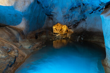 Stunning cave interior featuring a tranquil blue water pool, illuminated by natural light filtering through a rock opening, creating a serene and mystical atmosphere