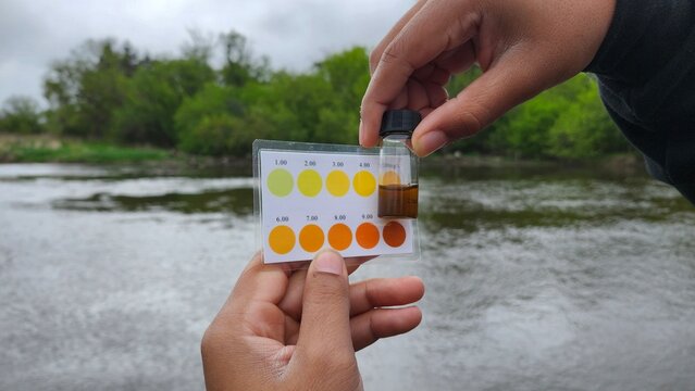 Hands holding a water sample and color chart for testing river water quality. Field testing for environmental monitoring or science education.