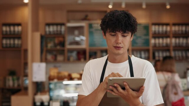 Portrait of attentive male server taking order with tablet computer in cafe. Young man uses digital menu working with guests in restaurant. Positive guy cafeteria employee