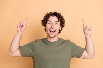 Excited young man with curly hair in casual green shirt pointing upwards with vibrant energy on...