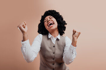 Joyful businesswoman in elegant attire celebrating success with cheerful smile and raised fists on...