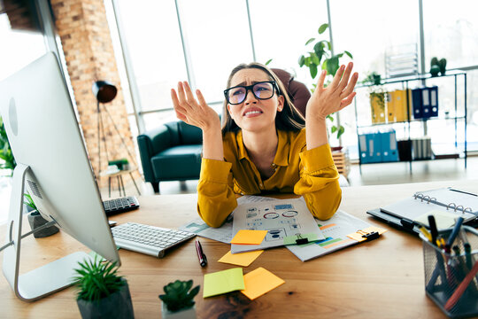Qualified female professional feeling overwhelmed at modern office desk with documents and computer on a well lit workspace