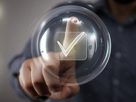 A man interacts with a futuristic transparent touchscreen interface, pressing a glowing virtual checkmark icon with his index finger