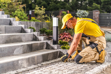 Construction Professional Laying Stone Pavers in Outdoor Landscape During Sunny Day in Residential Area