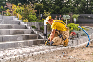 Skilled Worker Laying Cobblestones for a Garden Pathway in a Landscaped Area During Sunny Afternoon