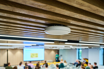 modern conference room with ceiling-mounted smoke detector, featuring wooden panels and a blurry...
