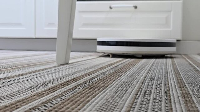Robot vacuum cleaner moving around the floor, passing by chair legs. Smart home cleaning in action, showcasing daily automated cleaning routine in a cozy interior.

