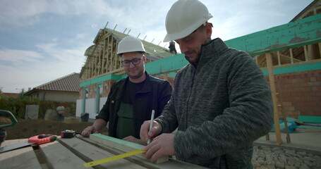Experienced builders measuring and marking wood with pencil and tape measure on a construction...