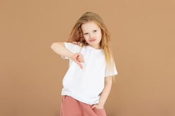Young sad displeased unhappy girl wear white t-shirt showing thumb down dislike gesture isolated on...
