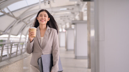 Businesswoman in office attire holding coffee cup while commuting in the urban business district.