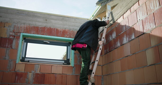 Worker descending ladder on building site, teamwork and safety focus, completing work on residential structure, construction project outdoors