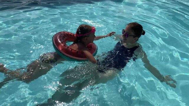 a little girl swims in the pool next to her mother and kisses her