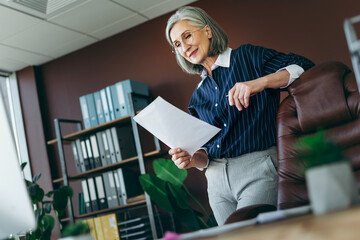 Confident mature businesswoman in a professional office setting analyzing documents, showcasing leadership and executive style