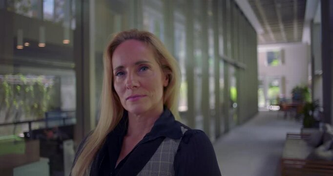 Woman standing still in corridor with intense direct gaze, conveying authority confidence and assertiveness in modern work environment