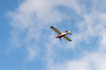 Classic airplane flying high in the blue sky on a clear day with white clouds above an open...