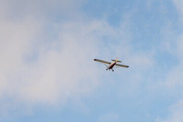 Small aircraft flying through a partly cloudy sky during daylight in a serene landscape