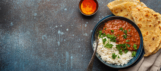 Traditional Indian Punjabi dish Dal makhani with lentils and beans in black bowl served with basmati rice, naan flat bread, fresh cilantro and spoon on blue concrete rustic table top view. Copy space.