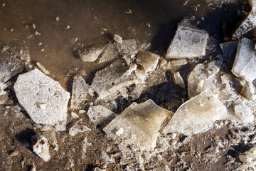 Melting crushed ice on dirt road. Details shot. Abstract background of melted spring ice close up.