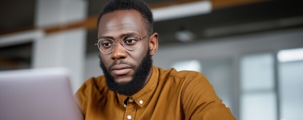 Obraz premium Focused african male adult working on laptop in modern office setting