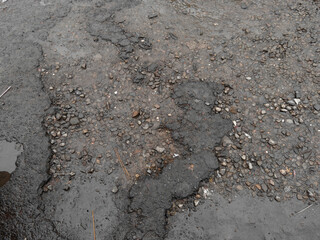 Damaged asphalt road with exposed gravel and wet surface after rain in urban area