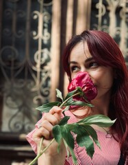 Woman with red hair enjoys flower while embracing nature in urban setting on a warm afternoon