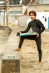 Surfer wearing wetsuit holding surfboard on beach