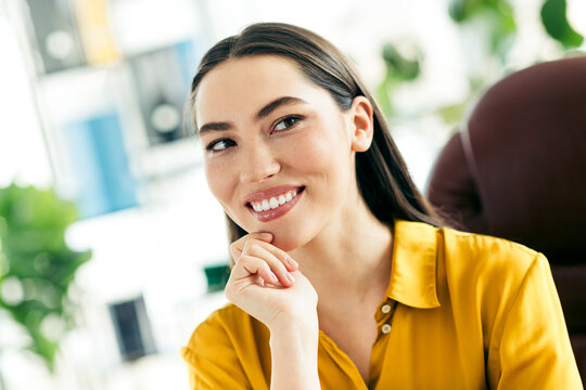 Confident businesswoman in casual attire smiling in a modern office setting, representing entrepreneurial spirit and professional charm
