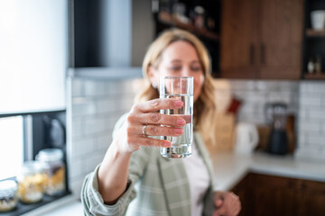 Woman holding glass of fresh water in kitchen promoting hydration and healthy lifestyle