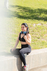 A young woman rests and relaxes with her eyes closed, sitting in the park, after exercising and playing sports