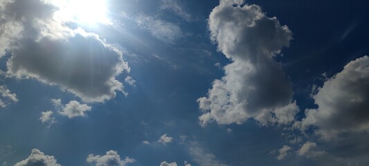 White multi-level clouds. Snow-white fluffy cumulus and translucent cirrus clouds in the light blue sky. They are located at different heights. The bright sun shines from behind the cloud.