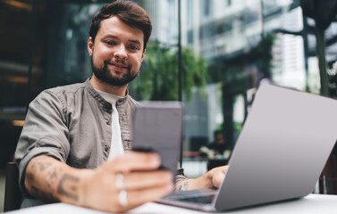 Fototapeta premium Man types on laptop at outdoor café with modern glass facade, showing freelancer lifestyle in Kuala Lumpur business district