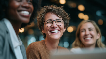 Obraz premium Close-up of three diverse business women smiling and talking in an office setting, highlighting the joyous moment as they interact with each other. The focus is on their faces, 