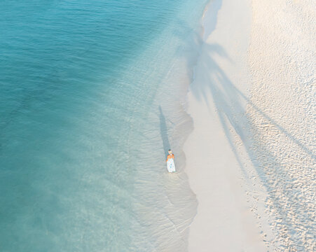 Aerial view of a beautiful tropical beach with a woman relaxing under the palm tree shadow, Alif Alif Atoll, Thoddoo, Maldives.