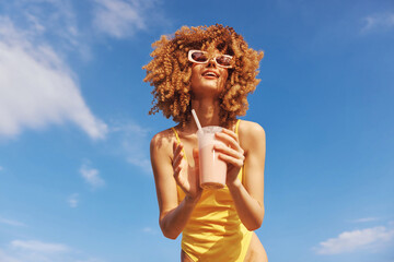 Young woman enjoying a refreshing drink in a vibrant summer outfit against a clear blue sky