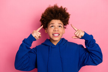 Happy teenager in blue hoodie making gestures with both hands against light pink background with bright expression