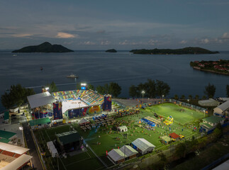 Mahé, Seychelles - 04 May 2025: Aerial view of a vibrant sports field and tents during an evening festival by the ocean, Roche Caiman, Mahe, Seychelles.