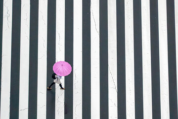 Tokyo City, Japan - 21 March 2021: Aerial view of a bustling zebra crossing with a pink umbrella amidst rushing pedestrians, Tokyo City, Tokyo Prefecture, Japan.