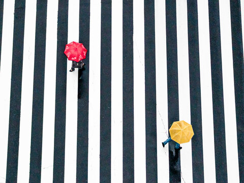 Tokyo City, Japan - 21 March 2021: Aerial view of a busy zebra crossing with red and yellow umbrellas and two people rushing to cross, Tokyo City, Tokyo Prefecture, Japan.