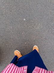 An overhead shot focusing on a person's feet in brown sneakers, wearing a navy blue skirt and a...