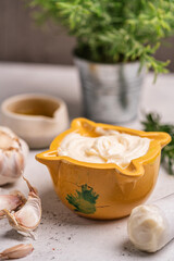 Homemade aioli or allioli garlic sauce in a special mortar on a table with the pestle on the side and ingredients the garlic, olive oil and salt