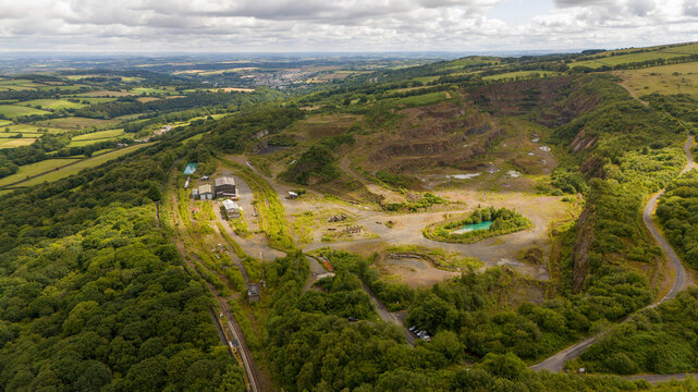 Aerial view of an abandoned quarry with a tranquil pool surrounded by lush greenery and hills, Meldon, England.