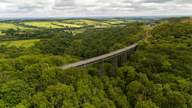 Aerial view of lush Meldon viaduct spanning a tranquil valley surrounded by serene woodland, Okehampton, United Kingdom.