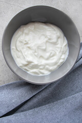 Gray bowl with white natural yogurt on the stone marble table.