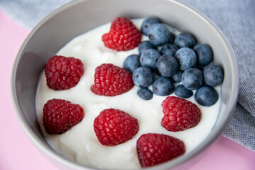 Gray bowl and natural yogurt with red and blue berries on the pink background.