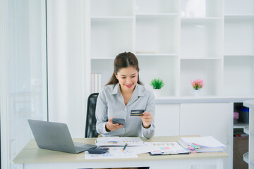 Beautiful Asian woman using smartphone buying online shopping by credit card while wear sweater sitting on desk in living room at home. Lifestyle woman at home concept.