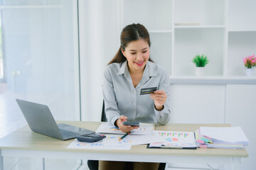 Portrait Asian woman using credit card with mobile phone, laptop for online shopping in modern lobby or working space, coffee cup, technology money wallet and online payment concept,credit card mockup