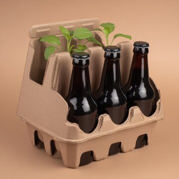 Three dark beer bottles in recycled cardboard holder with green sprouts studio shot on beige background