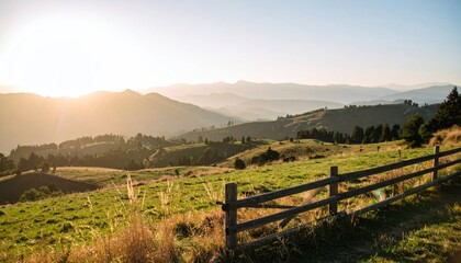 Rolling hills meet mountains at sunset, with a grassy field and wooden fence