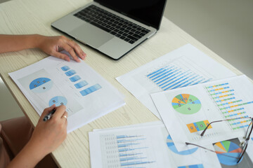 An asian business woman is using laptop at office and checking the financial graph reports showing results about the investment and planning process of her successful real estate business growth on.