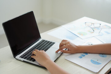 An asian business woman is using laptop at office and checking the financial graph reports showing results about the investment and planning process of her successful real estate business growth on.	
